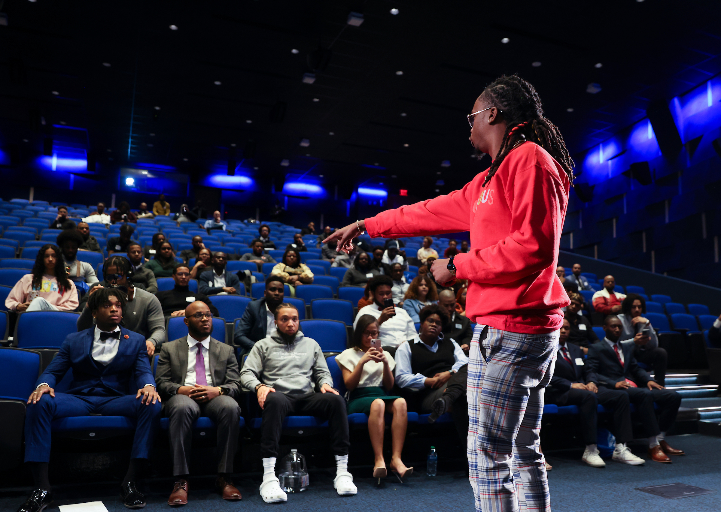 Man on stage in red sweater giving talk to auditorium of students