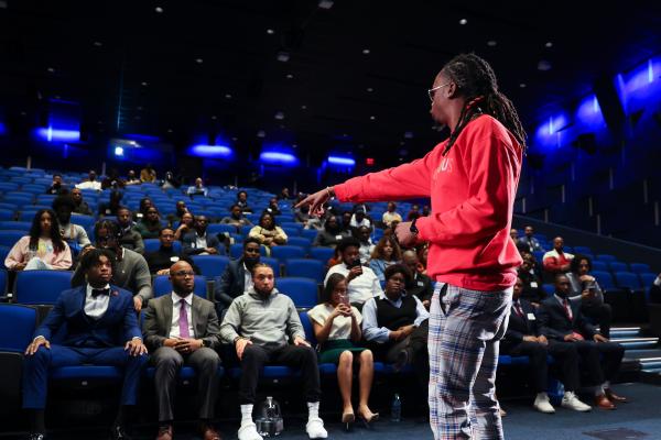 Man on stage in red sweater giving talk to auditorium of students