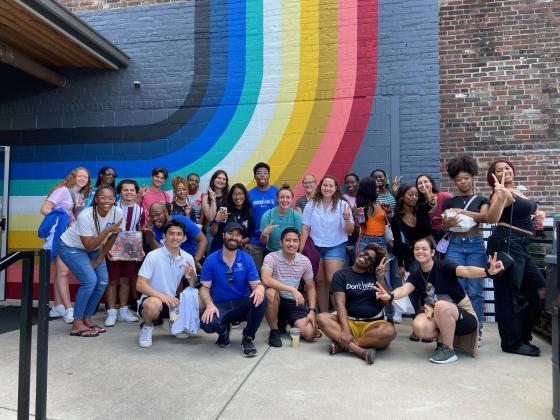 group of students smiling in front of rainbow mural