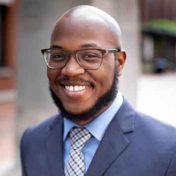 Headshot of man outside wearing navy blazer and glasses