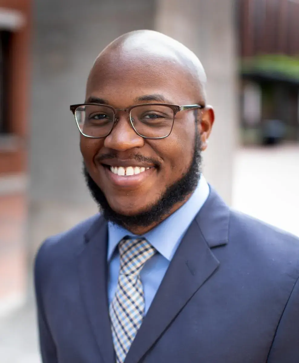 Headshot of man outside wearing navy blazer and glasses