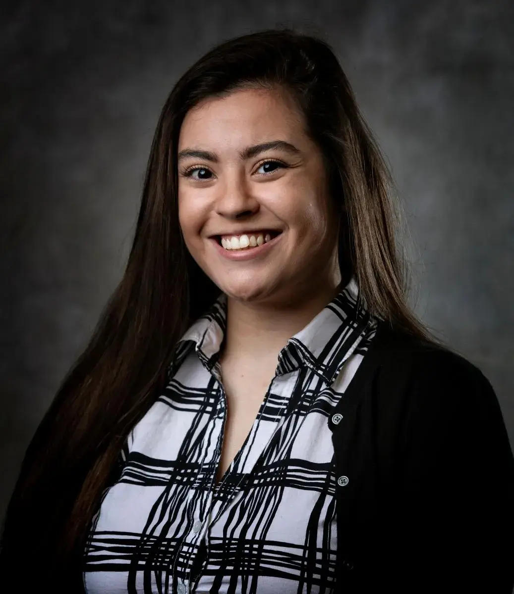 headshot of woman in black and white plaid shirt with black sweater